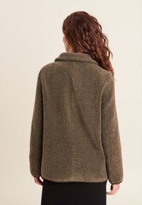 Braune Fleece-Jacke mit hohem Kragen, langen Ärmeln und lässiger Passform. Weiche Textur, glatte Oberfläche und keine sichtbaren Verschlüsse oder Verzierungen.