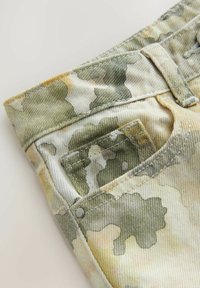 Kamouflage-mönstrad denimtyg i grön och beige, med en liten bakficka och metallnitar på midjebandet.