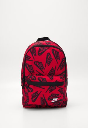 Sac à dos rouge couvert de logos Nike noirs, poche avant zippée et boucle de poignée noire sur fond blanc uni.