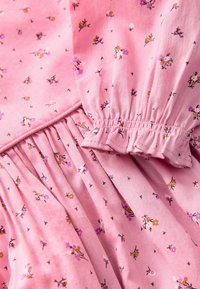 Tessuto di cotone rosa con piccoli motivi floreali in viola e giallo. Presenta maniche arricciate e un design plissè per una maggiore texture.