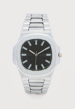 Hõbedast metallist randmekell musta ruudukujulise sihverplaadiga, valgete tunniindeksite ja kolmeosalise näiduga, mis näitab aega 10:10:30.