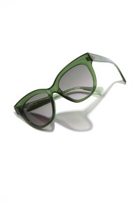 Ochelari de soare cu tentă verde, rame mari în formă de ochi de pisică, lentile cu gradient și brațe transparente. Prezintă un branding subtil pe tija ochelarilor.