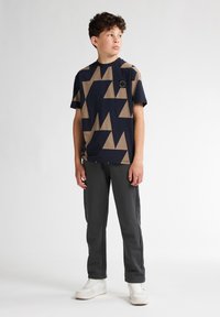 Mörkblå t-shirt med tan geometriskt mönster, kortärmad, rund hals; matchad med grå sweatpants och vita sneakers.