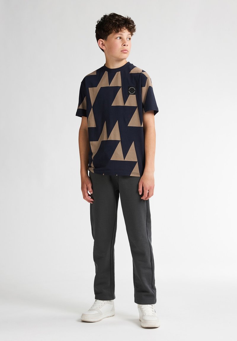 Mörkblå t-shirt med tan geometriskt mönster, kortärmad, rund hals; matchad med grå sweatpants och vita sneakers.