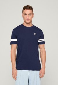 Camiseta de algodón azul marino con mangas cortas y rayas blancas, y un escote redondo. Pequeño logo en el pecho, corte casual.
