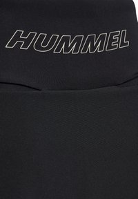 Musta kangas, jonka yläosassa valkoisella ääriviivalla kuvattu "HUMMEL"-logo, joka esittää rakennetta ja ompelun yksityiskohtia.