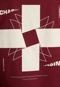 Medžio spalvos marškinėliai, puoštos geometriniu baltu raštu su persidengiančiomis linijomis ir tekstu. Minkšta medžiaga su lygia tekstūra. Minimalistinis stilius.