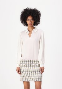 White blouse with pleated sleeves and a V-neckline, paired with a multicolored tweed mini skirt featuring button accents and frayed hem.