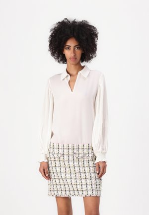 White blouse with pleated sleeves and a V-neckline, paired with a multicolored tweed mini skirt featuring button accents and frayed hem.
