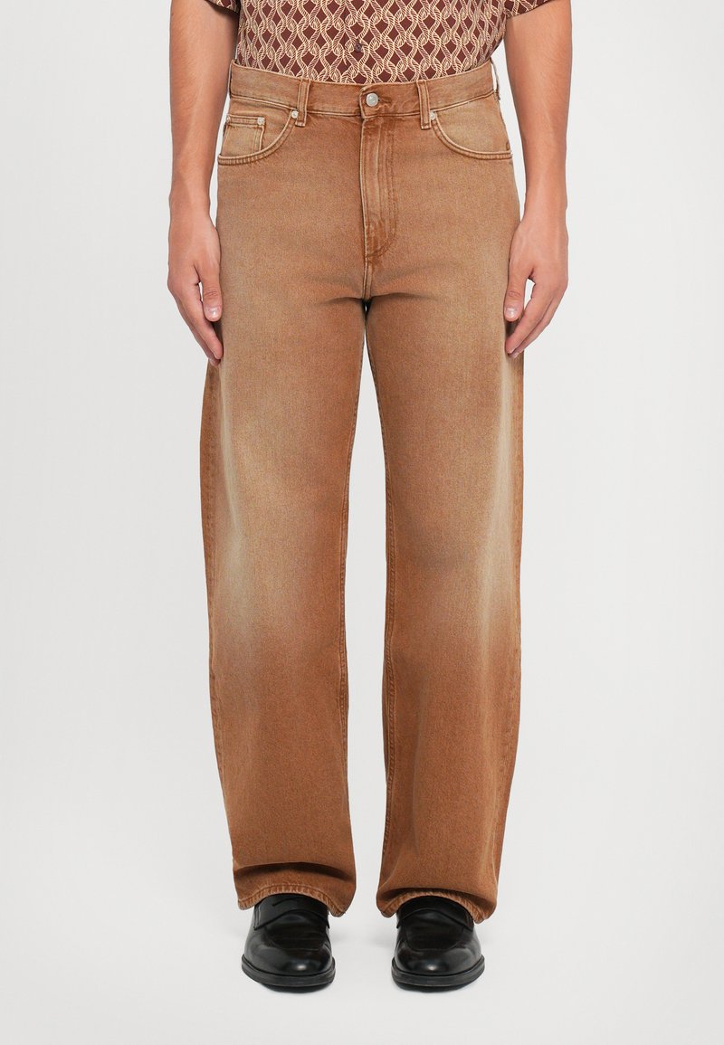 Brune denimjeans med en løs pasform, der har en klassisk knap- og lynlåslukning og fem lommer, parret med sorte sko.