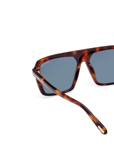 Okulary przeciwsłoneczne w kolorze skorupy żółwia z kwadratowymi szkłami i niebieskim przyciemnieniem. Gładkie plastikowe oprawki z wąskimi brązowymi zausznikami. Złoty akcent na zauszniku.