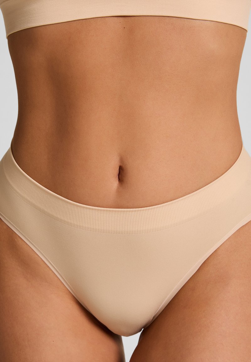 Naadloze huidkleurige slipjes met een zachte, elastische tailleband. Soepele textuur en hoog uitgesneden beenontwerp, wat zorgt voor een comfortabele pasvorm.