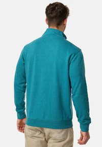 Suéter turquesa con cuello alto, mangas largas y puños acanalados. Textura suave con un diseño limpio y sencillo. Costuras visibles en los hombros.