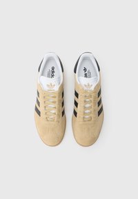 Αθλητικά παπούτσια από σουέντ σε μπεζ χρώμα με τρεις μαύρες ρίγες. Διαθέτουν λευκά κορδόνια και μαλακή λευκή εσωτερική επένδυση. Λαστιχένια σόλα με ανάγλυφο πέλμα.