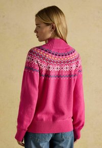 Pleteni pulover v svetlo roza barvi, ki ima vzorčasto yoko z belimi in večbarvnimi poudarki, rebrast ovratnik in rob ter dolge rokave.