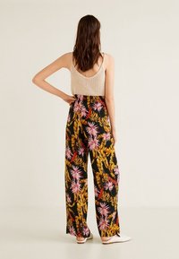 Pantaloni neri a gamba larga con un motivo floreale tropicale in rosa, giallo e verde, abbinati a un top in maglia beige chiaro. Tessuto in misto cotone.