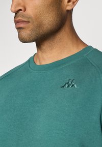 Teal katoenen sweatshirt met een ronde hals en geborduurd logo op de borst. Zachte textuur, licht getailleerd ontwerp.