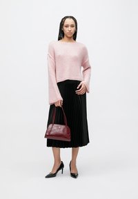 Pink knitted cropped sweater with long bell sleeves, paired with a black pleated skirt and a burgundy leather handbag. Black high heels.