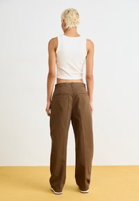 Pantalon marron à jambes larges et taille haute, avec deux poches arrière. Porté avec un débardeur blanc côtelé ajusté. Design simple et minimaliste.