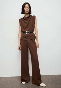 Top tricotat maro fără mâneci cu un gât drapat, asociat cu pantaloni largi la talie înaltă. Accesorizat cu o curea neagră cu o fibie argintie.
