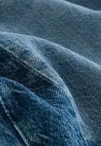 Denimtyg i olika nyanser av blått, som visar en texturerad yta med synliga vävmönster och subtila blekningseffekter.