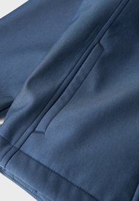 Tessuto blu navy con una texture liscia, caratterizzato da una tasca laterale e dettagli di cucitura puliti. Il design è elegante e formale.
