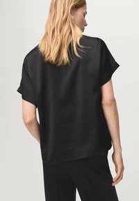 Czarna satynowa bluzka z krótkimi rękawami, o luźnym kroju i gładkiej fakturze. Charakteryzuje się lekko zaokrąglonym dołem i minimalistycznym designem.