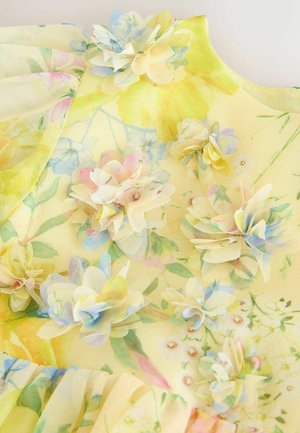 Žluté květinové šaty s průsvitnou vrstvou, zdobené látkovými květinami v pastelových odstínech a jemnými vzory zeleně po celém povrchu.