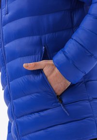 Giubbotto piumino blu con design a intreccio orizzontale, tasche con zip e una texture liscia e lucida. Presenta polsini a costine e una zip completa.