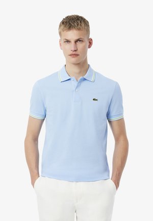Polo azzurro chiaro in misto cotone, caratterizzato da un colletto classico, maniche corte con accenti a strisce verdi e bianche, e un piccolo logo.