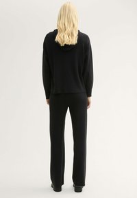 Schwarzer gestrickter Kapuzenpullover kombiniert mit passenden weit geschnittenen Hosen; bietet eine weiche Textur und einen lässigen Schnitt, von hinten gesehen.