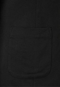 Černá bavlněná tkanina se čtvercovou kapsou a viditelným stehem, vystihující hladkou texturu a jednoduché designové prvky.