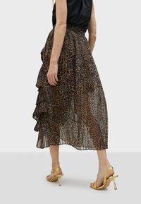 Hame midi semitransparan bercorak macan tutul dengan lapisan berkerut, terbuat dari kain ringan. Dipadukan dengan sepatu hak tinggi ber tali metalik emas.