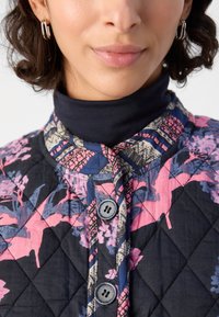 Quilted Jacke in Dunkelblau mit lebhaften Blumenmustern in Pink und Türkis. Verfügt über einen Stehkragen und zwei graue Knöpfe auf der Vorderseite.