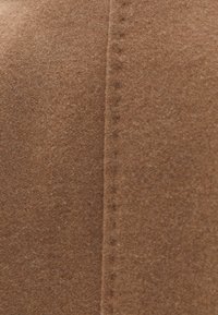 Hnědý filcový materiál s měkkou texturou, který má viditelné švy podél švu. Povrch vykazuje mírnou načechranost a má rovnoměrnou barvu.