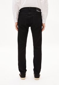 Jean en denim noir avec une coupe droite, présentant des poches arrière, une étiquette sur la taille, et des détails de chaussures contrastants.