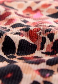Leopard print fabric with a ribbed texture features shades of tan, black, red, and pink in a wavy, soft drape.