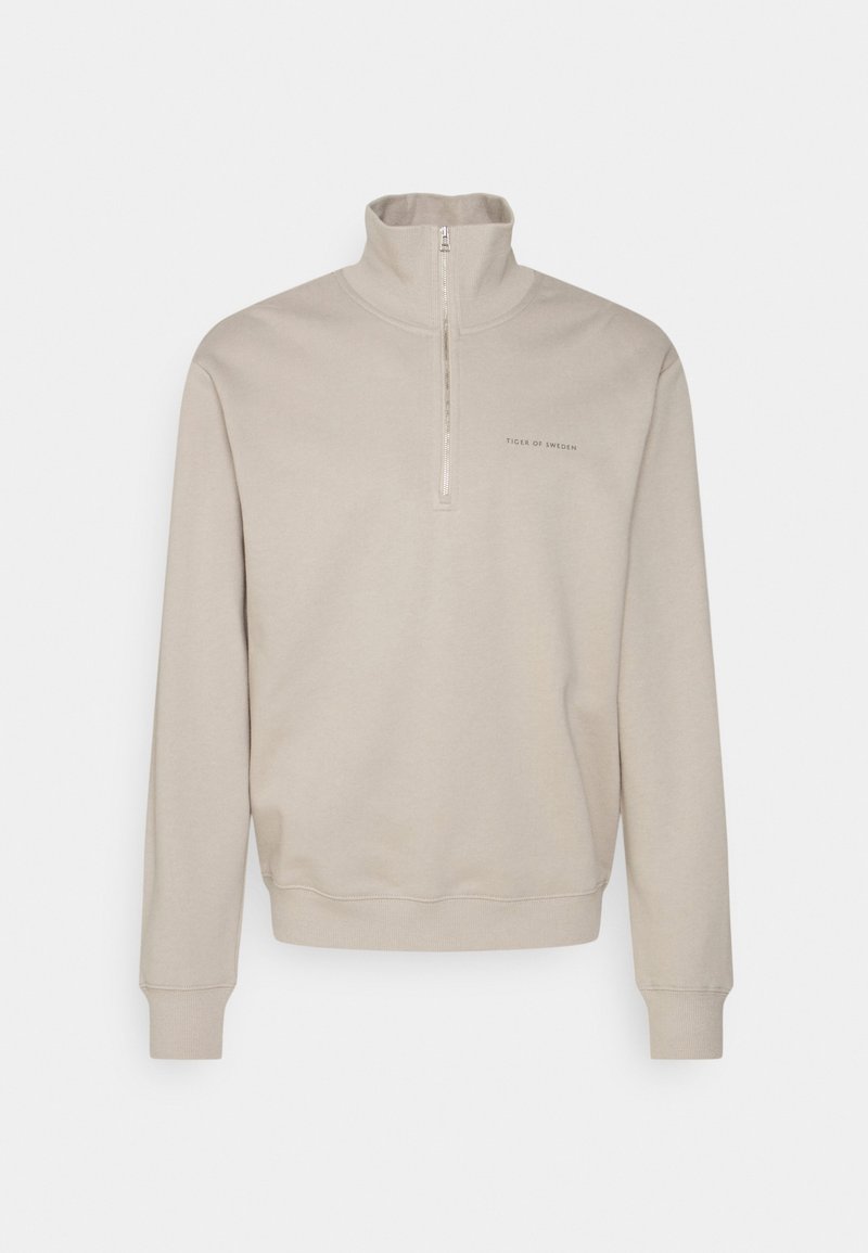 Beige halvdraget sweatshirt i mjuk bomull, med ståkrage, ribbade muddar och en minimalistisk logotyp på bröstet.