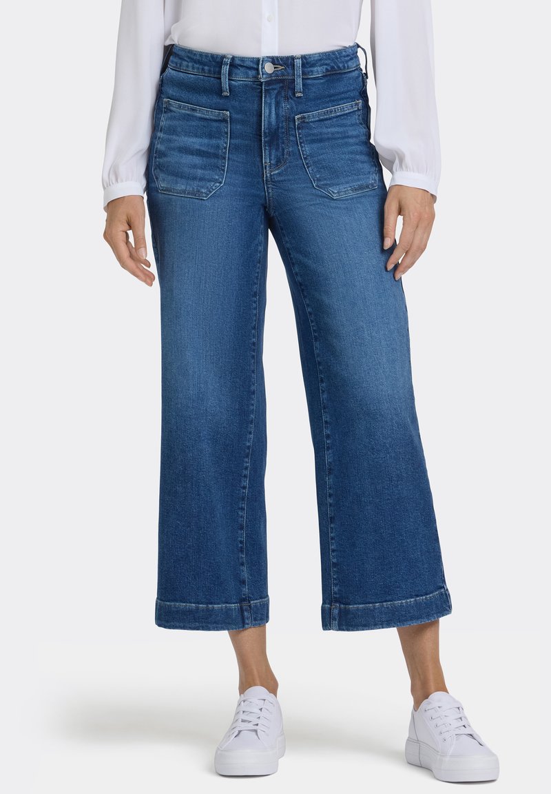 Vida denimjeans i mellanblått med fram- och bakfickor, avslutade med uppvikta fållar. Bärs med vita sneakers.