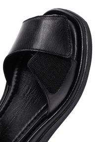 Sandal nera con tomaia in pelle liscia, dotata di una fascia ampia e chiusura regolabile in velcro. Suola piatta in gomma con trama sottile.