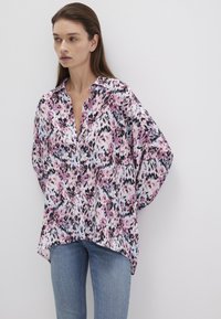 Blumenbluse in lila, rosa und schwarzen Tönen, aus leichtem Stoff gefertigt. Sie hat eine lockere Passform, lange Ärmel und einen klassischem Kragen mit Knöpfen.