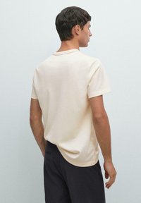 Kortærmet, creamfarvet t-shirt med rund halsudskæring og subtil syning på ryggen, parret med mørke shorts.