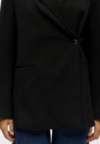 Juoda švarkas turi vieno mygtuko užsegimą, aštrius reketus ir dvi priekines kišenes. Pagamintas iš lygaus audinio su pritaikytu siluetu.