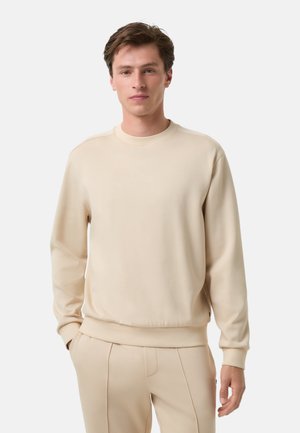 Beżowa bluza wykonana z miękkiego materiału, z okrągłym dekoltem, długimi rękawami oraz ściągaczami na rękawach i u dołu. Prosty, minimalistyczny design.