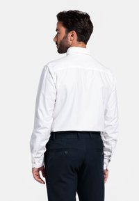 Witte overhemd met lange mouwen, knoopsluiting en een klassieke kraag, in een getailleerde pasvorm met enkele knopen bij de manchetten, gecombineerd met donkere, op maat gemaakte broek.