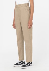 Beige vysoké kalhoty s plochým předním dílem, bočními kapsami a páskem v pase. Odpovídají černobílým šněrovacím teniskám.