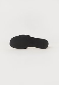 Semelle de chaussure noire avec surface en caoutchouc texturée et motif de crampons léger. Présente une forme arrondie et un design plat sans logo visible.