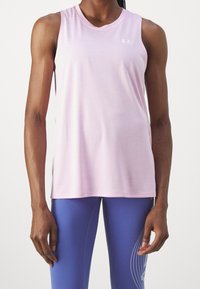 Top deportivo de color rosa claro, hecho de una tela suave, con un escote redondo y un logo en la parte superior izquierda. Se usa con leggings azules.