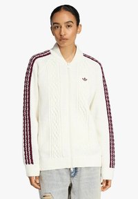 Maglione bianco lavorato a maglia con motivo a treccia, cerniera completa, polsini e orlo a coste. Presenta strisce bordeaux e logo sul petto a sinistra.