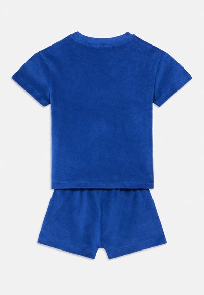 Modrý bavlnený dvojdielny set z froté materiálu, pozostávajúci z trička s krátkym rukávom a šortiek. Hladká textúra s rebrovaným výstrihom a lemami.